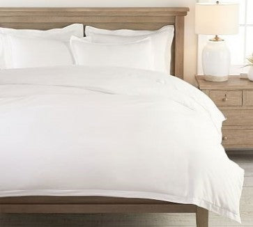 White bedding set on a wooden bed with a lamp in the background