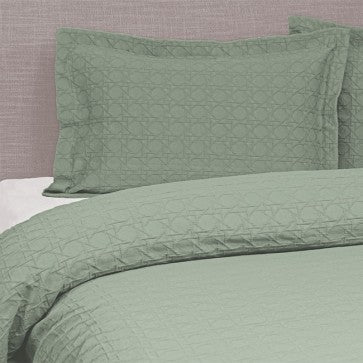 Green quilted bedspread and pillow on a bed with a neutral background