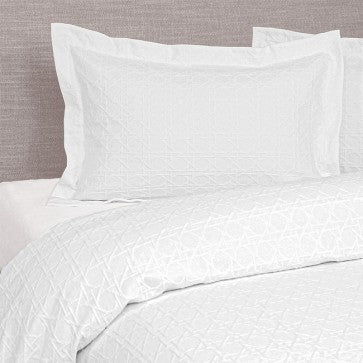 White bedding set with pillows on a bed against a neutral headboard.